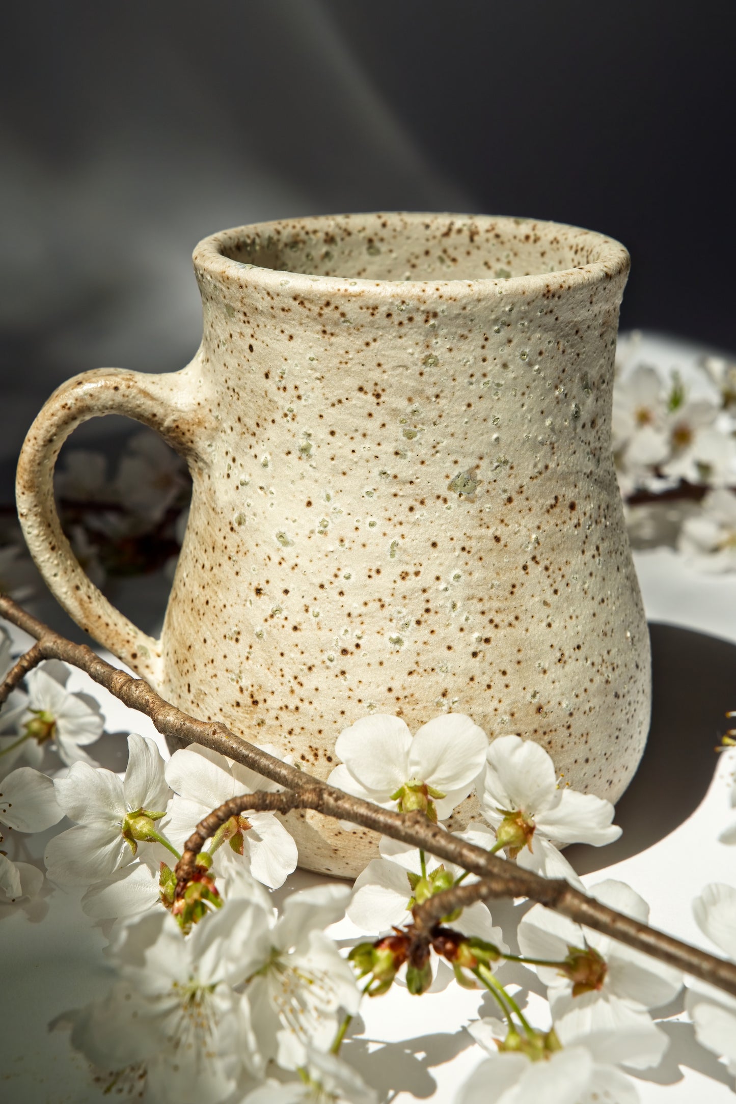 Speckled ceramic mug with tiny green crystals on a surface with cherry blossoms