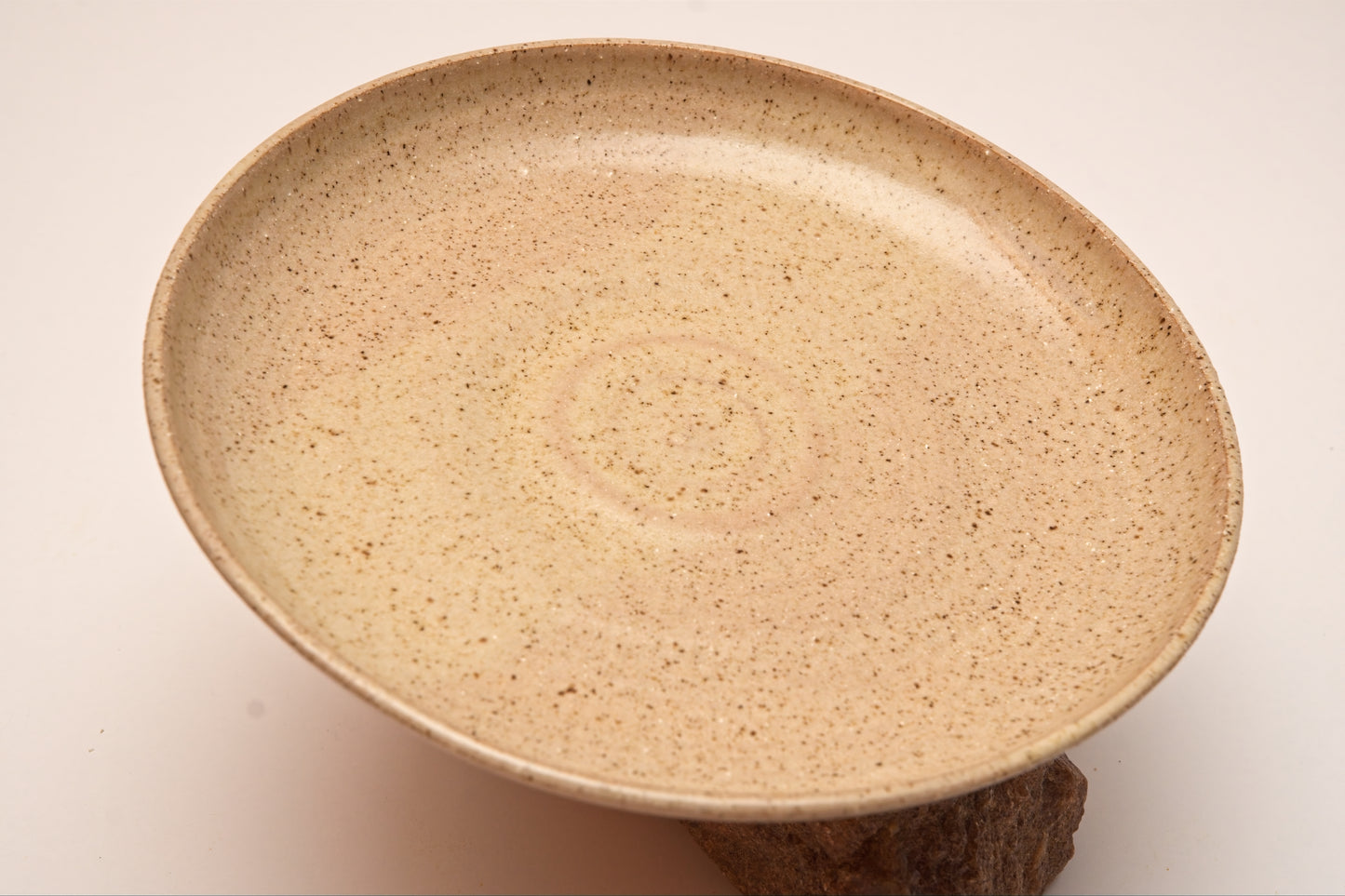 Beige ceramic plate with speckled clay sitting atop a rock against a light beige background