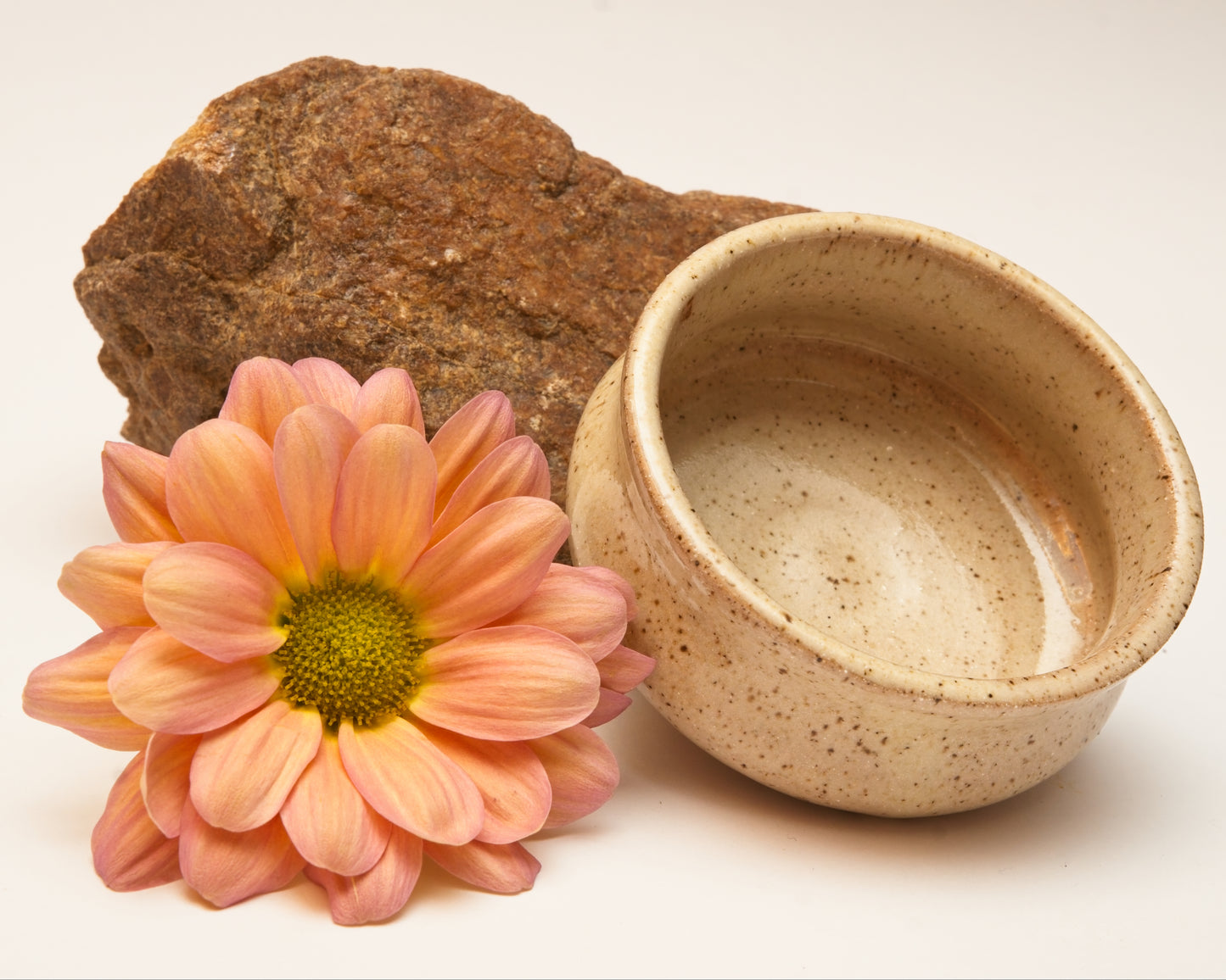 Ceramic copita, pink flower, and rock on a white background