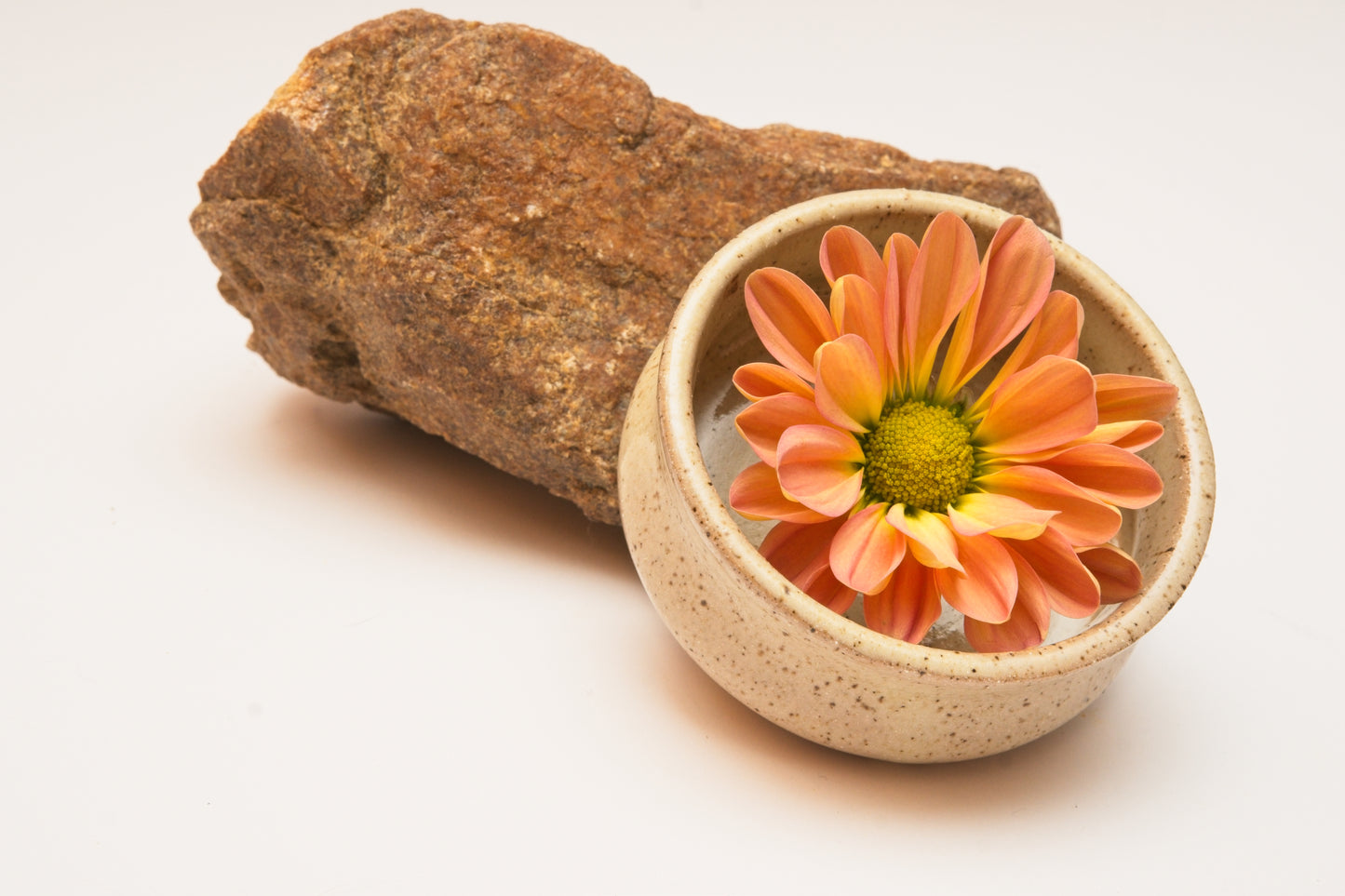 Ceramic copita drinking glass with a pink flower inside, next to a rock on a light background