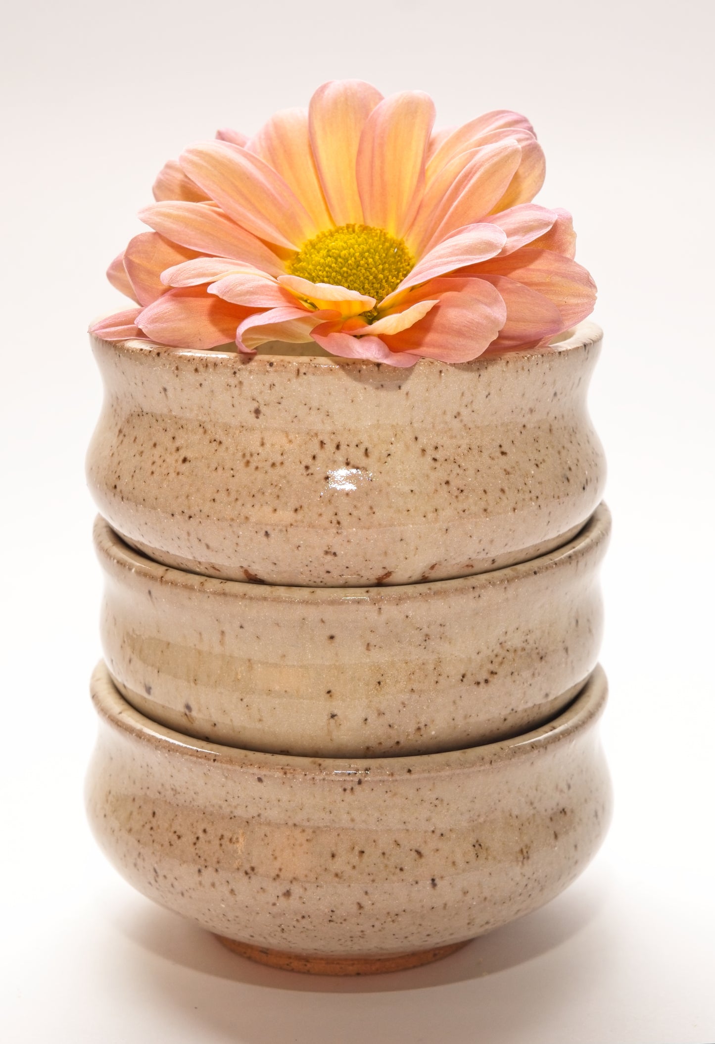 Stack of three beige ceramic copita glasses with a pink flower on a white background