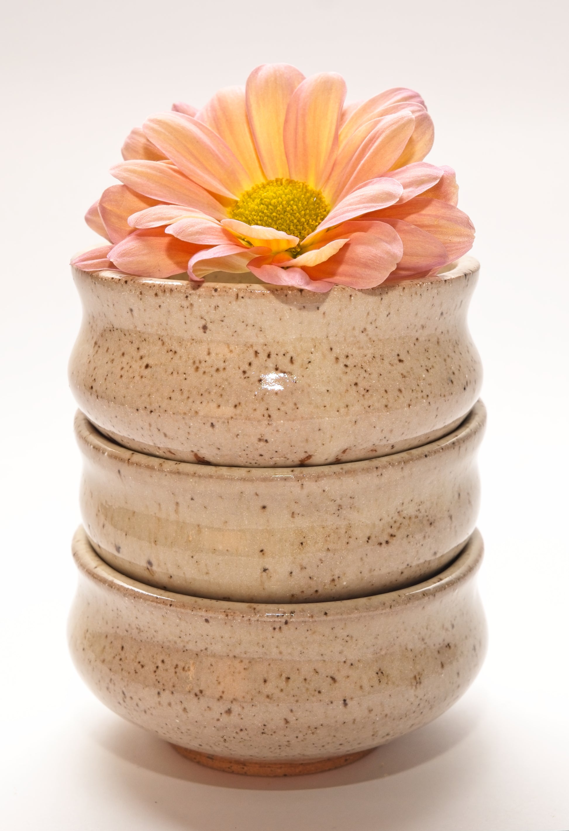 Stack of three beige ceramic copita glasses with a pink flower on a white background