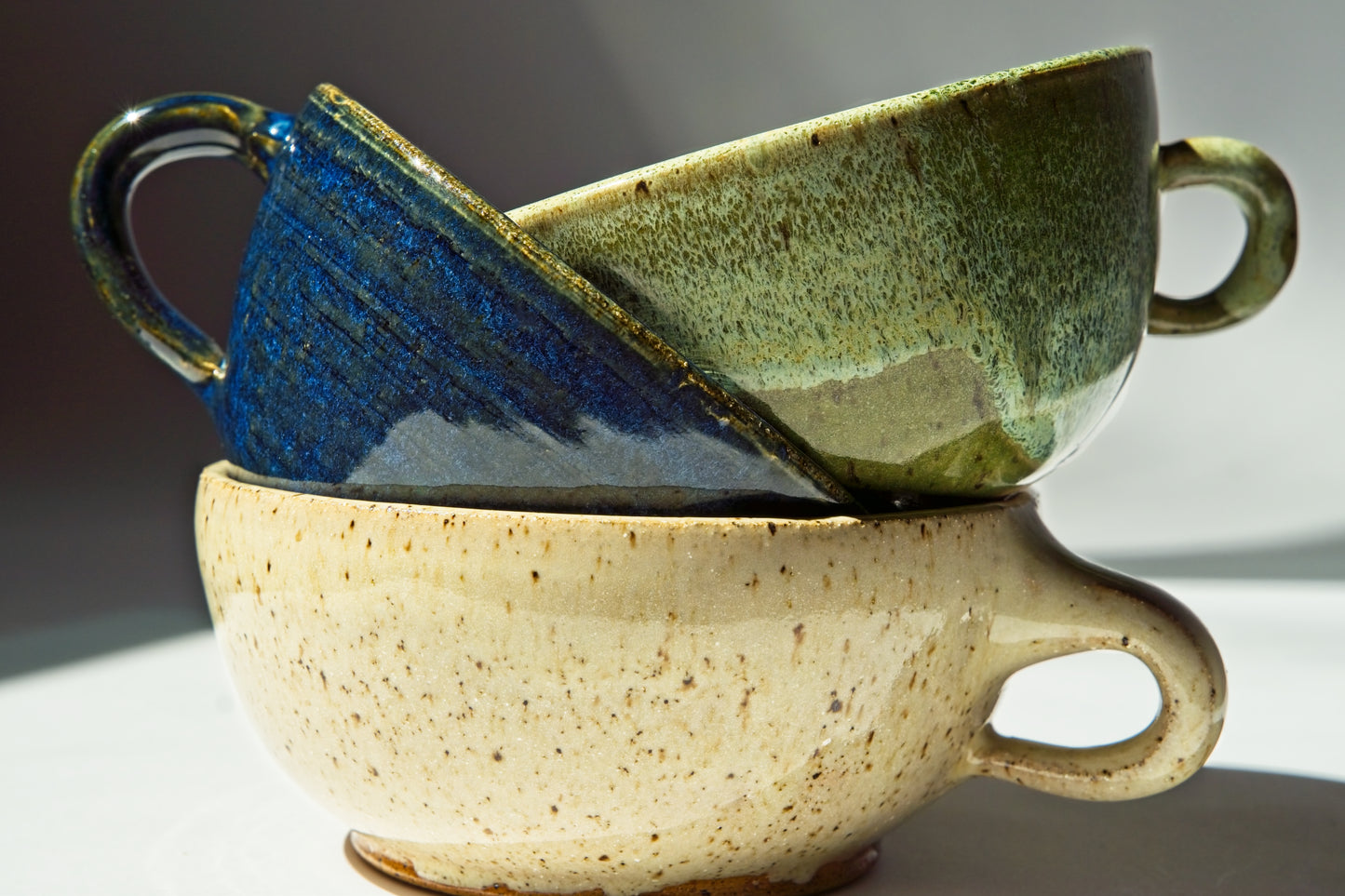 Three small ceramic espresso mugs of different colors stacked on a reflective surface with a gradient background.