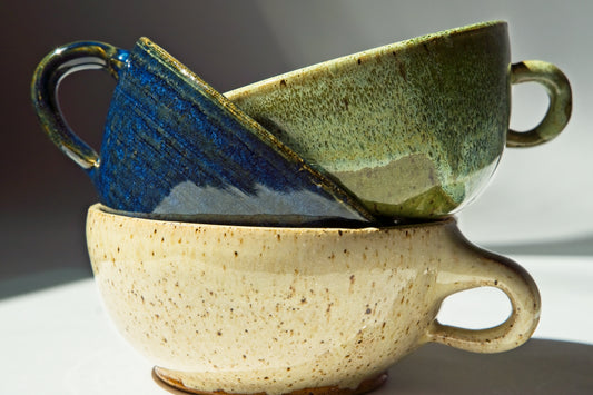Three small ceramic espresso mugs of different colors stacked on a reflective surface with a gradient background.