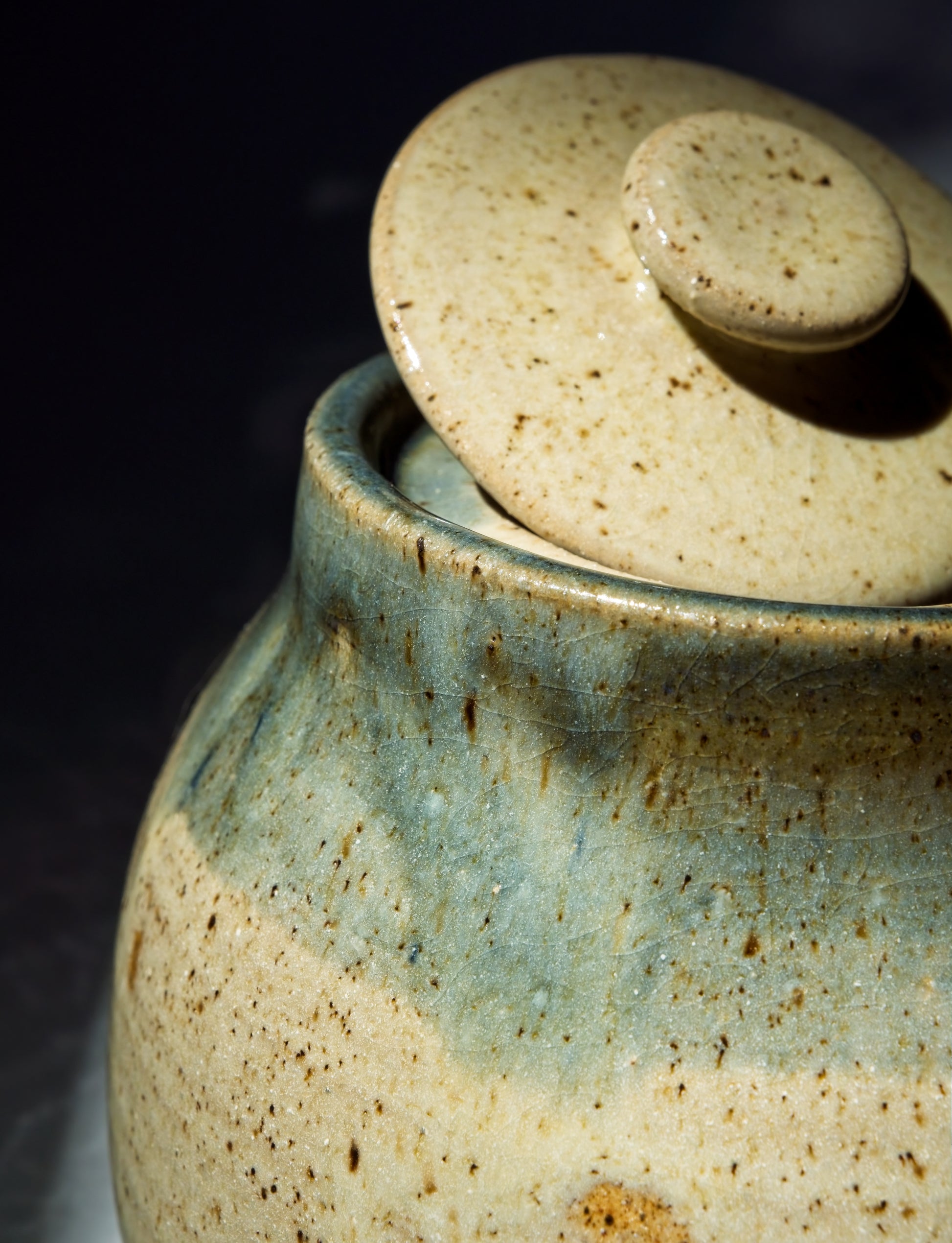 Beige and crackly blue glaze stoneware jar with a lid on a dark background