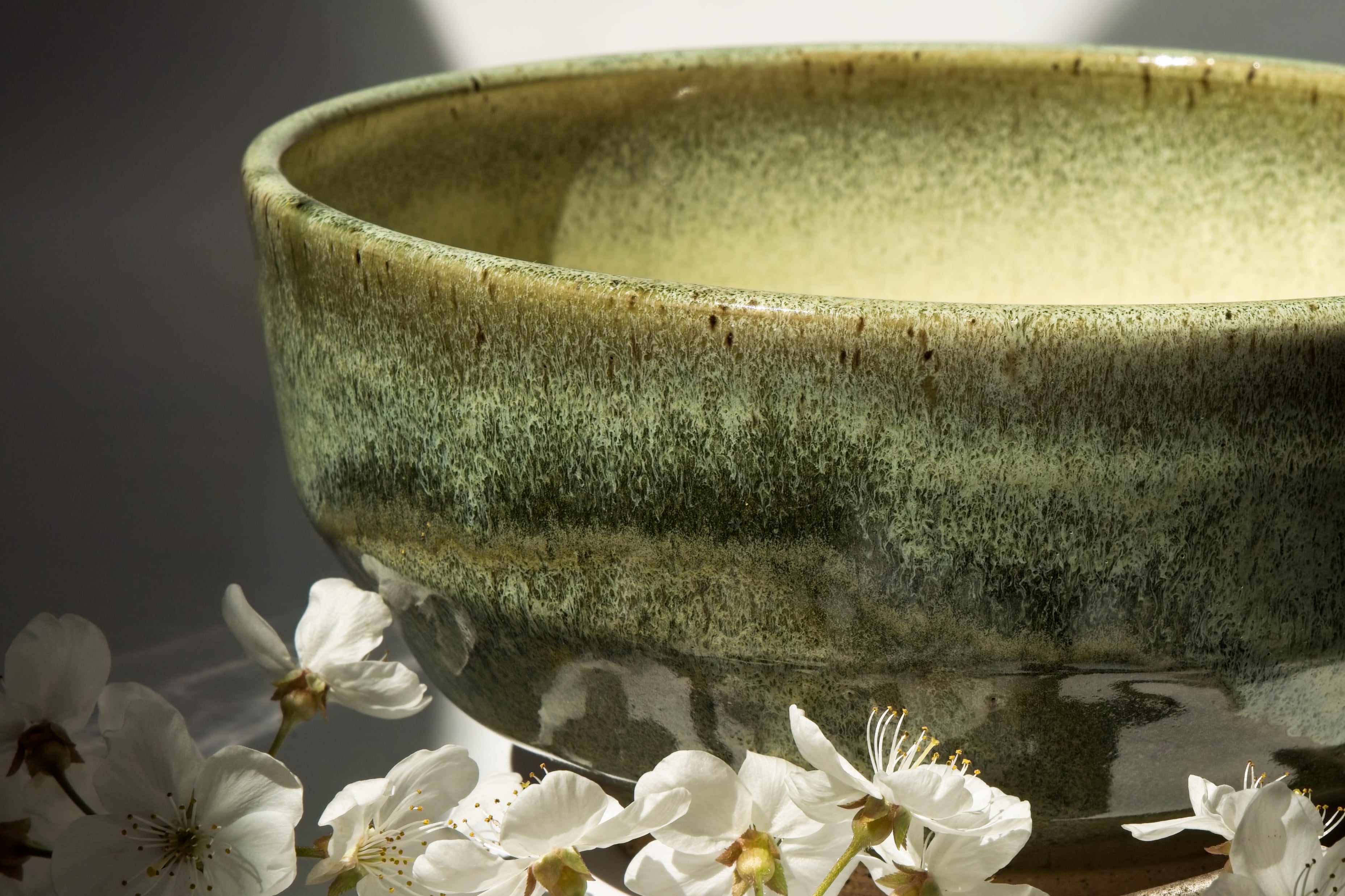 large ceramic bowl with reflective green glaze against white flowers on a white surface