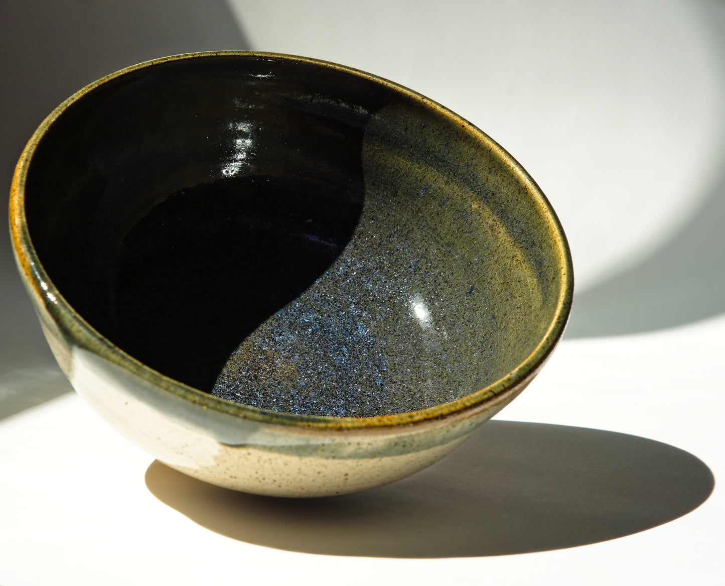 Large ceramic bowl with dark blue interior and speckled exterior on a white background