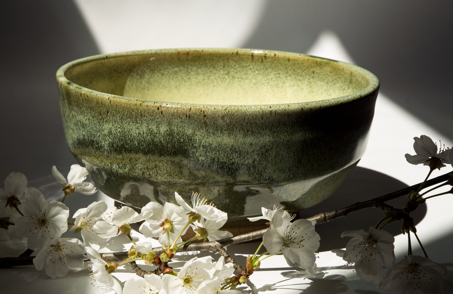 Large green ceramic bowl with cherry blossoms on a light background