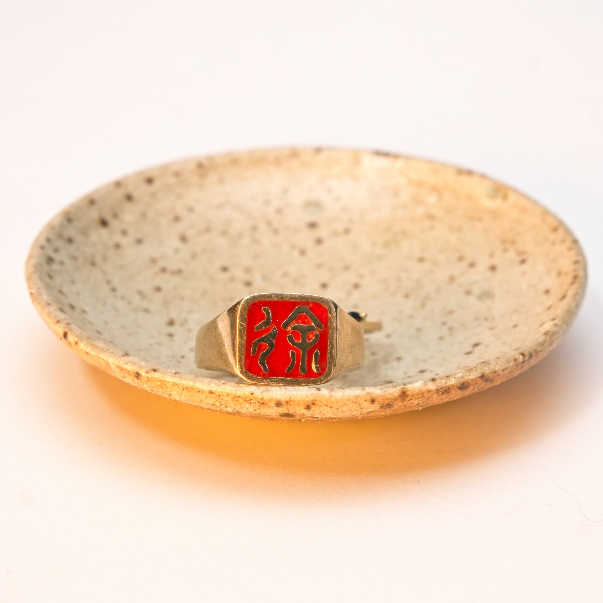 Gold ring with red emblem on a speckled ceramic dish