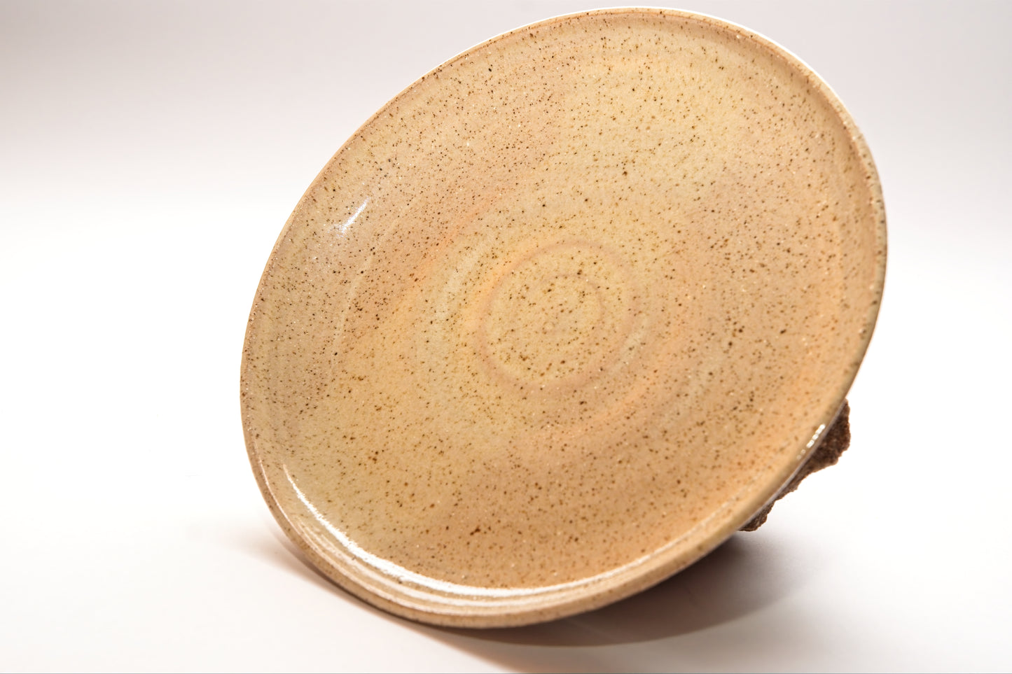 Small beige ceramic plate with speckled clay on a white background